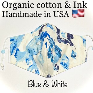 May include: A white face mask with a blue and white abstract print. The mask is made of organic cotton and ink and is handmade in the USA. The text "Blue & White" is printed below the mask.