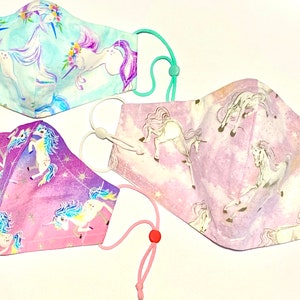 May include: Three unicorn-themed face masks with elastic ear loops. The masks are made of cotton fabric and feature a variety of unicorn designs in pink, purple, and blue.