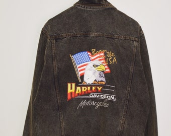 May include: Black denim jacket with an embroidered Harley Davidson logo featuring an eagle and American flag. The logo reads "Born in the USA" and "Harley Davidson Motorcycles".