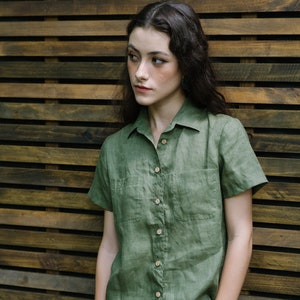 May include: A green linen shirt with short sleeves and a button-down collar. The shirt has two pockets on the front and a relaxed fit.