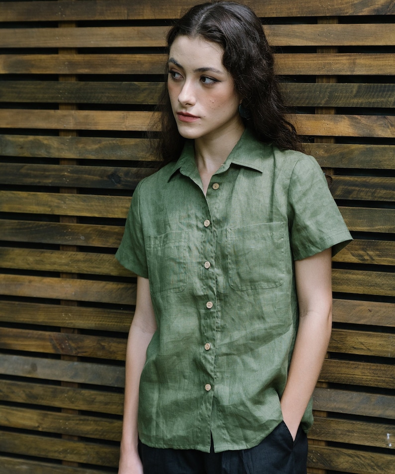 May include: A green linen shirt with short sleeves and a button-down collar. The shirt has two pockets on the front and a relaxed fit.