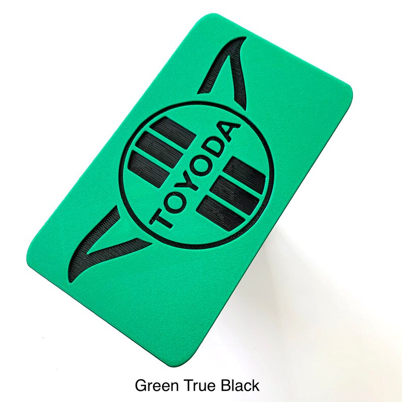 K&ouml;nnte beinhalten: Ein rechteckiger, gr&uuml;ner Gegenstand mit dem schwarzen Wort "TOYODA". Der Text befindet sich in einem schwarzen Kreis mit schwarzen Linien. Die Oberfl&auml;che ist strukturiert und der Text "Green True Black" steht unten.