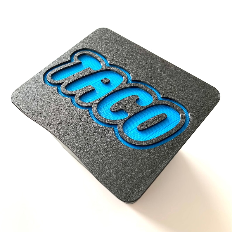 May include: A black square-shaped sign with the word "Taco" in blue raised lettering.