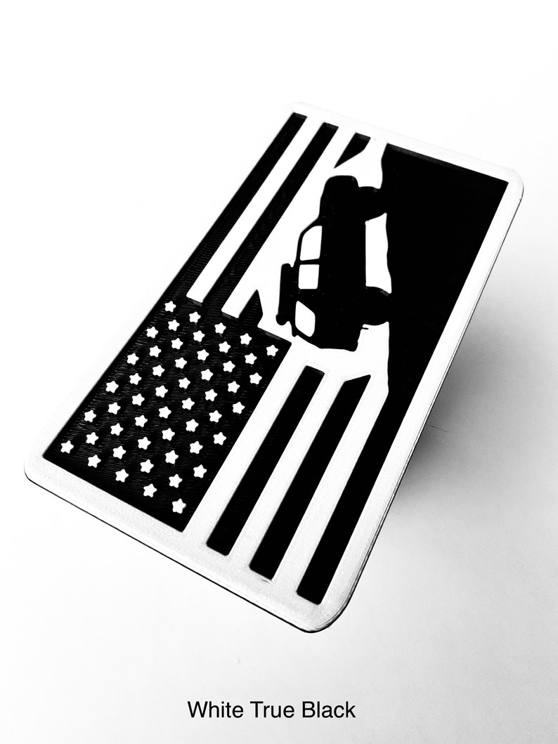 May include: A black and white American flag with a silhouette of a jeep driving over a hill. The flag is on a white background.