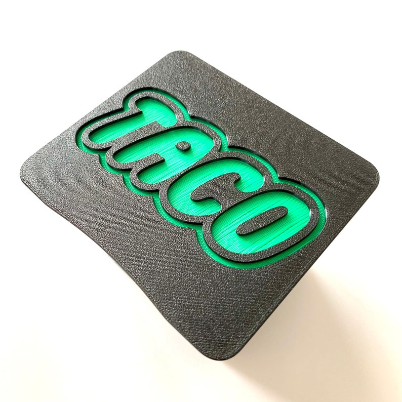 May include: A black and green sign with the word "Taco" in a 3D, bubble-like font.