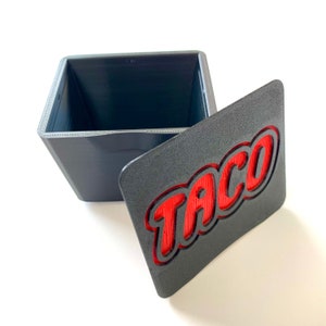 May include: A gray box with a red "Taco" inscription on the lid. The box is open and the inside is empty.