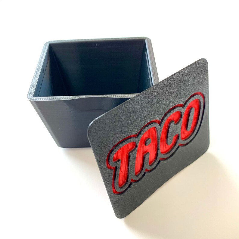 May include: A gray box with a red "Taco" inscription on the lid. The box is open and the inside is empty.