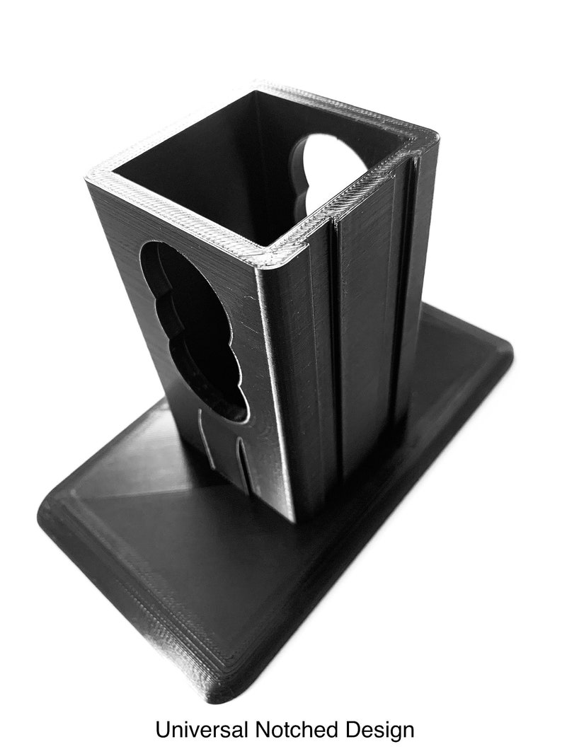 May include: A black 3D printed phone stand with a notched design. The stand has a rectangular base and a square top with a cutout for a phone.
