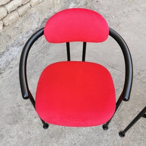 May include: A red upholstered chair with a black metal frame. The chair has a rounded back and a circular seat.