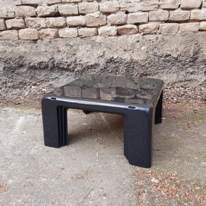 May include: A black, rectangular coffee table with a glossy finish and a unique, layered design. The table is made of plastic and has a modern, minimalist style.