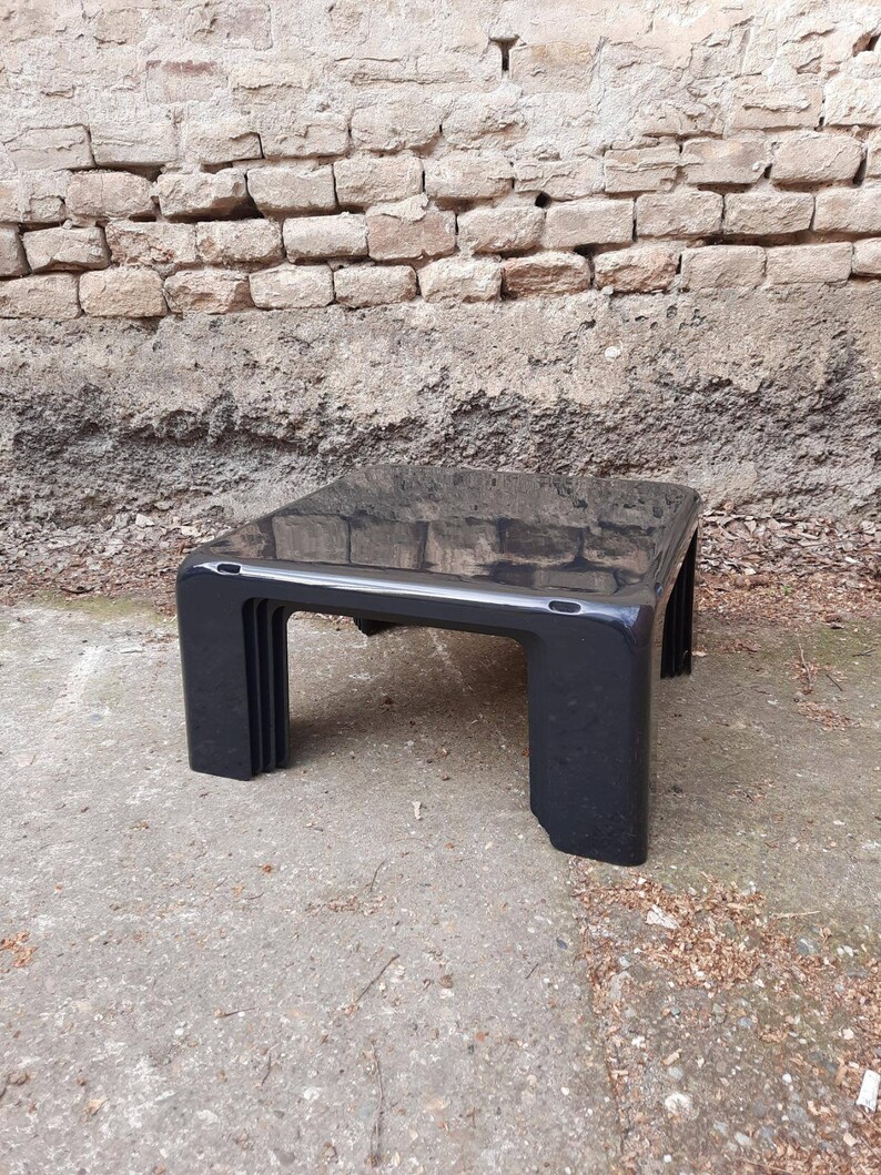 May include: A black, rectangular coffee table with a glossy finish and a unique, layered design. The table is made of plastic and has a modern, minimalist style.