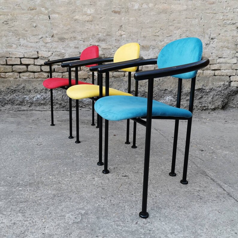 May include: Four chairs with black metal frames and colorful fabric seats. The chairs are arranged in a row, with the blue chair in the foreground and the red chair in the background.
