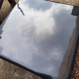 May include: A black, glossy, square-shaped table top with a reflection of the sky in it.