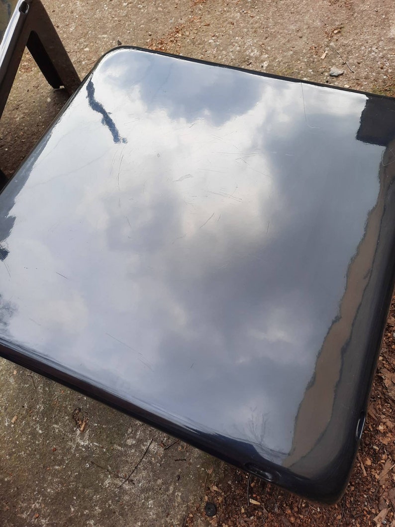 May include: A black, glossy, square-shaped table top with a reflection of the sky in it.