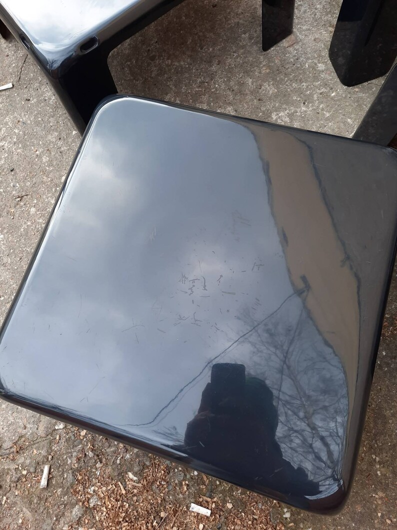 May include: Two black plastic chairs with a glossy finish. The chairs are square and have a simple design.