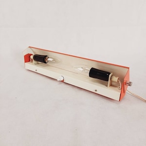 Peut inclure: Un luminaire mural vintage orange et blanc avec deux ampoules. Le luminaire a un design simple et un interrupteur blanc.