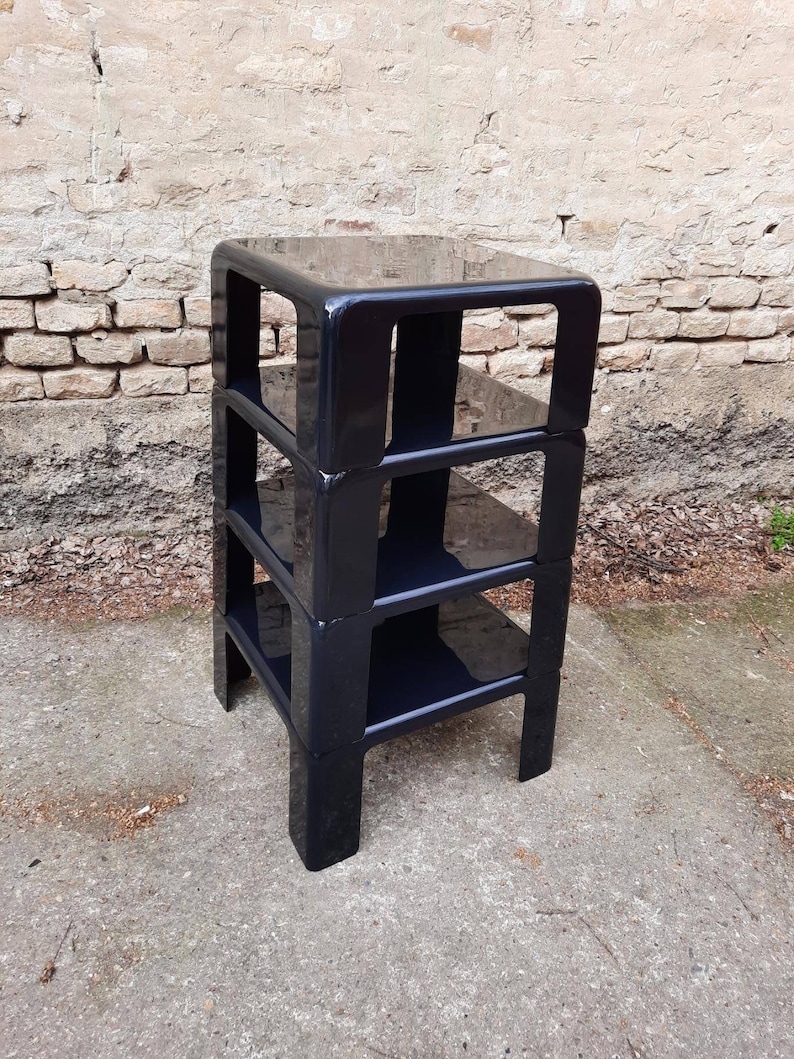 May include: A black, four-tiered, modular shelving unit made of plastic. The shelves are stacked on top of each other and have a glossy finish.