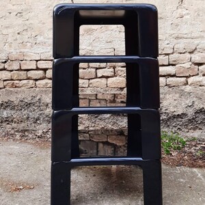 May include: A set of four black, stackable shelves made of plastic. The shelves are square and have a simple, modern design.