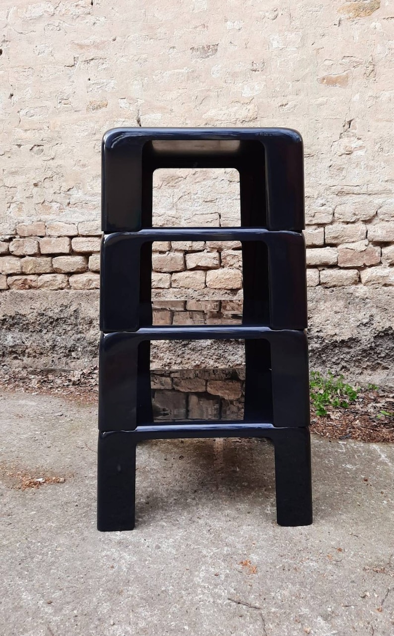 May include: A set of four black, stackable shelves made of plastic. The shelves are square and have a simple, modern design.