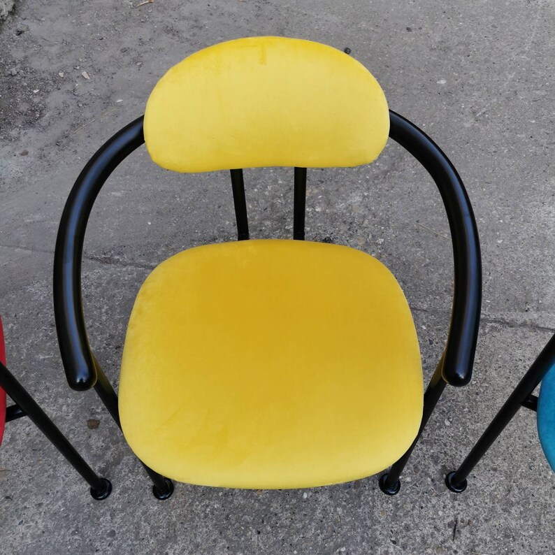May include: A yellow velvet chair with a black metal frame. The chair has a rounded back and a wide seat.