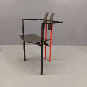 May include: A modern chair with a dark brown seat and frame. The chair features two vertical red supports and two dark brown back supports. The chair has a minimalist design and is set against a gray background.