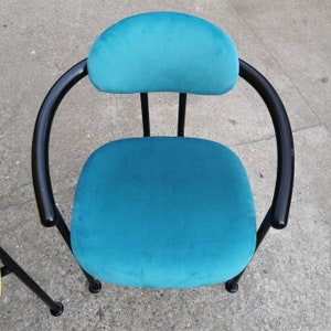 May include: A teal blue armchair with a black metal frame. The chair has a rounded back and a comfortable seat.