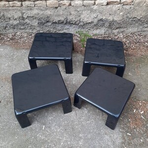 May include: Four black square nesting tables with a glossy finish. The tables are arranged in a staggered pattern on a gray concrete surface.