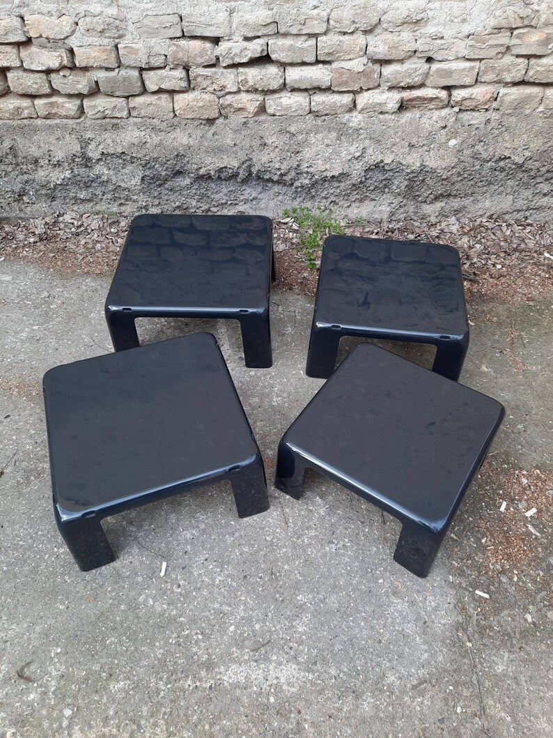 May include: Four black square nesting tables with a glossy finish. The tables are arranged in a staggered pattern on a gray concrete surface.