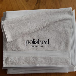 Folded grey embroidered towel with a small tonal embroidered word, wrapped neatly for a clean, minimalist product shot.