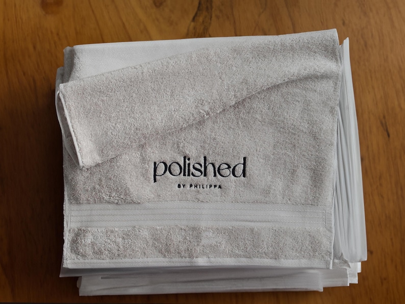 Folded grey embroidered towel with a small tonal embroidered word, wrapped neatly for a clean, minimalist product shot.