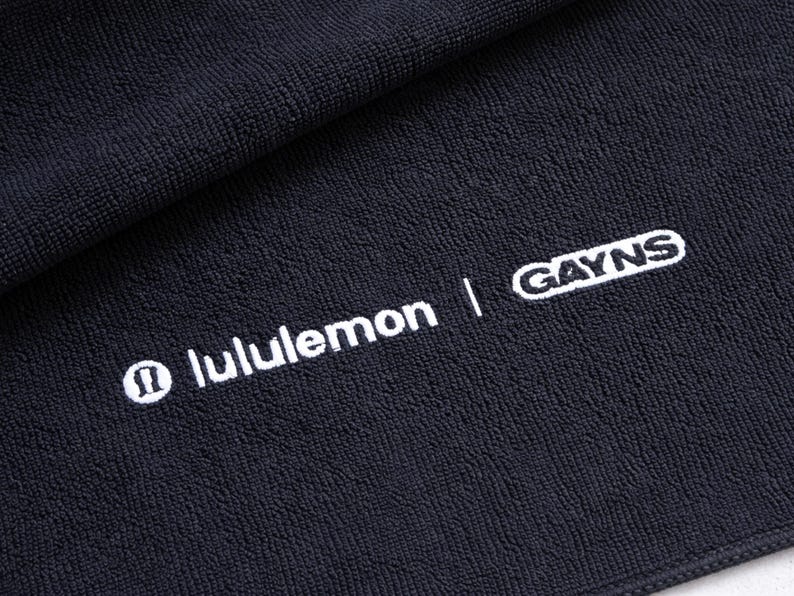 Black embroidered towel featuring a bold white wordmark-style design, a striking high-contrast look suited to modern business branding.