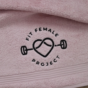 Blush pink embroidered towel featuring a circular fitness badge design with a heart and dumbbell icon, a fun personalised choice for a gym gift.