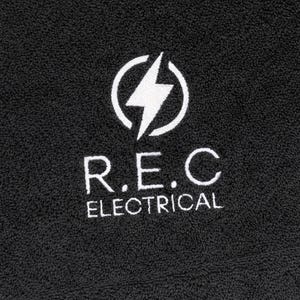 Charcoal textured towel with a circular badge emblem featuring a lightning bolt icon, embroidered in white thread for a bold, modern branding design.
