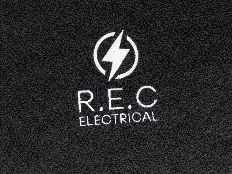 Charcoal textured towel with a circular badge emblem featuring a lightning bolt icon, embroidered in white thread for a bold, modern branding design.