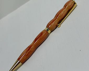 May include: A handcrafted wooden pen with a warm, reddish-brown finish and gold-colored accents. The pen features a unique, contoured design and a gold-colored clip and tip. The pen is a stylish writing instrument.