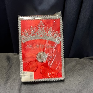 May include: Red satin keepsake box with a silver crown and rhinestones. The box has a silver border and the words "Mrs. To Be" are embroidered on the front. The box is $75.99.