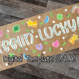 May include: A brown rectangular sign with the words "feelin' LUCKY!" in white and green lettering. The sign is decorated with colorful lucky charms, including rainbows, shamrocks, and hearts. The text "Digital Template ONLY!" is also present.