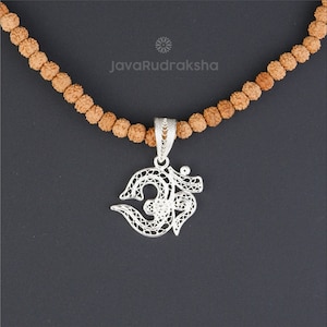 Pode incluir: Um colar com um pingente de Om de prata com um delicado design de filigrana, pendurado em uma corrente de contas marrons. A corrente é feita de contas de Rudraksha.