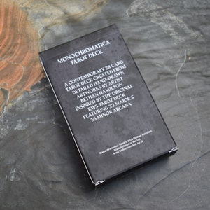 May include: A black box with white text that reads "Monochromatica Tarot Deck". The box features a description of the deck, which is a contemporary 78 card tarot deck created from detailed hand-drawn artworks by artist Bethan Hamilton. The deck is inspired by the original RWS Tarot deck and features 22 Major and 56 Minor Arcana.