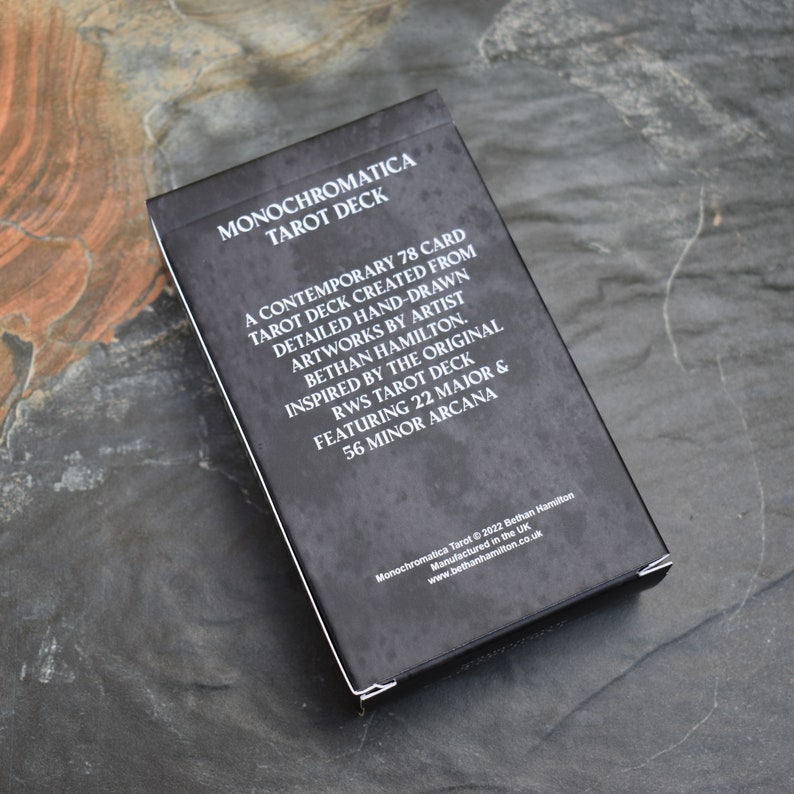 May include: A black box with white text that reads "Monochromatica Tarot Deck". The box features a description of the deck, which is a contemporary 78 card tarot deck created from detailed hand-drawn artworks by artist Bethan Hamilton. The deck is inspired by the original RWS Tarot deck and features 22 Major and 56 Minor Arcana.