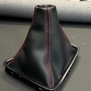 May include: Black leather gear shift boot with red stitching. The boot has a square base and a rounded top.