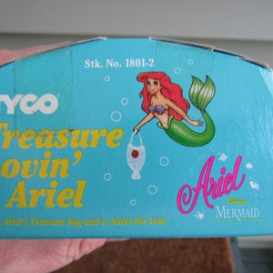 May include: A blue and yellow box with the text "TYCO Treasure Lovin' Ariel" and a picture of Ariel the mermaid from Disney's The Little Mermaid. The box also says "Stk. No. 1801-2" and "With Ariel's Treasure Bag and a Jewel for You!"