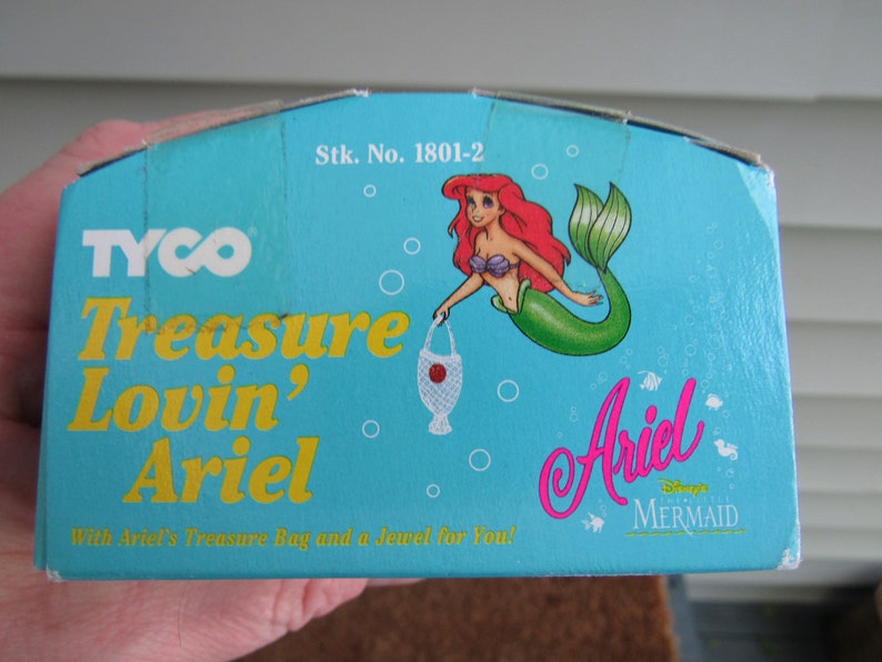 May include: A blue and yellow box with the text "TYCO Treasure Lovin' Ariel" and a picture of Ariel the mermaid from Disney's The Little Mermaid. The box also says "Stk. No. 1801-2" and "With Ariel's Treasure Bag and a Jewel for You!"