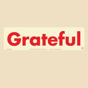 May include: A rectangular sticker with rounded corners, featuring the word "Grateful" in bold red letters. The sticker has a cream-colored background. The text "© 2023 PC850" and "Produced by Starshine Arts Inc. www.starshinearts.com" are also present.