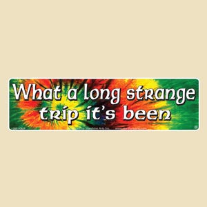 May include: A rectangular bumper sticker with the text "What a long strange trip it's been" in white letters. The background features a tie-dye design in shades of red, orange, yellow, and green.