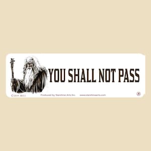 Puede incluir: Una pegatina rectangular blanca con el texto "YOU SHALL NOT PASS" en marrón, con una ilustración en blanco y negro de un mago sosteniendo un bastón. La pegatina también incluye el texto "©2019 JR511" y "Produced by Starshine Arts Inc."