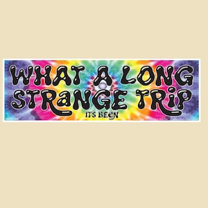 May include: A rectangular bumper sticker with the text "WHAT A LONG STRANGE TRIP IT'S BEEN" in black bubble letters. The background is a vibrant tie-dye pattern of pink, blue, yellow, and green.