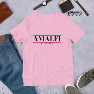 K&ouml;nnte beinhalten: Rosa T-Shirt mit schwarzem Text "AMALFI LA COSTIERA" mit gr&uuml;nen und roten Streifen &uuml;ber und unter dem Text.