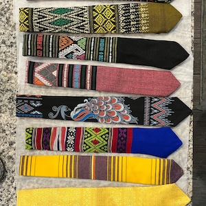 May include: A collection of 12 colorful patterned neckties. The ties feature a variety of designs, including geometric patterns, floral motifs, and sports themes. The ties are arranged in a row, with the most colorful tie at the top and the most simple tie at the bottom.