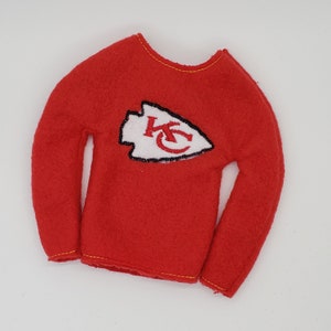 May include: Red long-sleeved elf shirt with a white and red "KC" arrowhead logo.